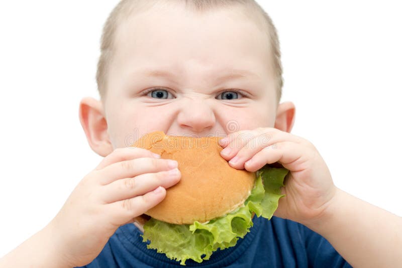 Close-up of a child biting a burger. Isolated photo, horizontal, the child looks into the frame. The idea is that kids