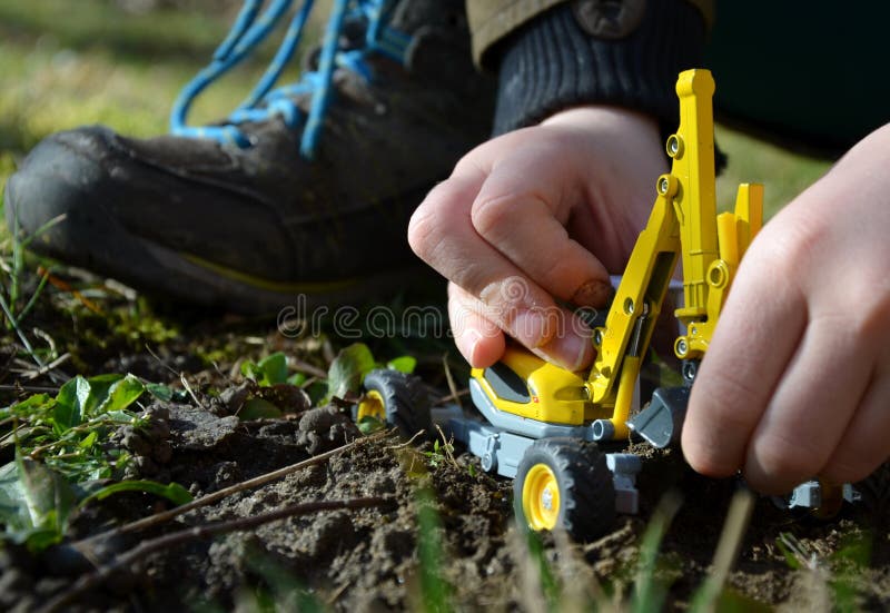 Close-up of child hands on playing in clay with yellow excavator grass boy white grass soil work play shoes