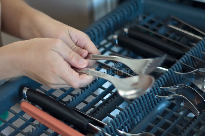 Close up child loading the dishwasher: holding a spoon and fork. High quality photo. Automatic loading stock images, royalty-free photos and pictures