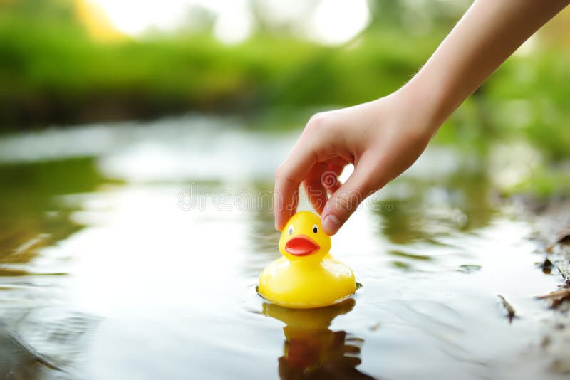 Close-up on childs hand playing by a river with rubber duck. Child having fun with water on warm summer day. Active family leisure