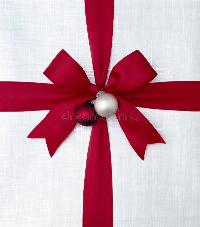 Close-up closeup of Christmas gift present with bright red satin ribbon bow and silver white wrapping paper. Simple, graphic