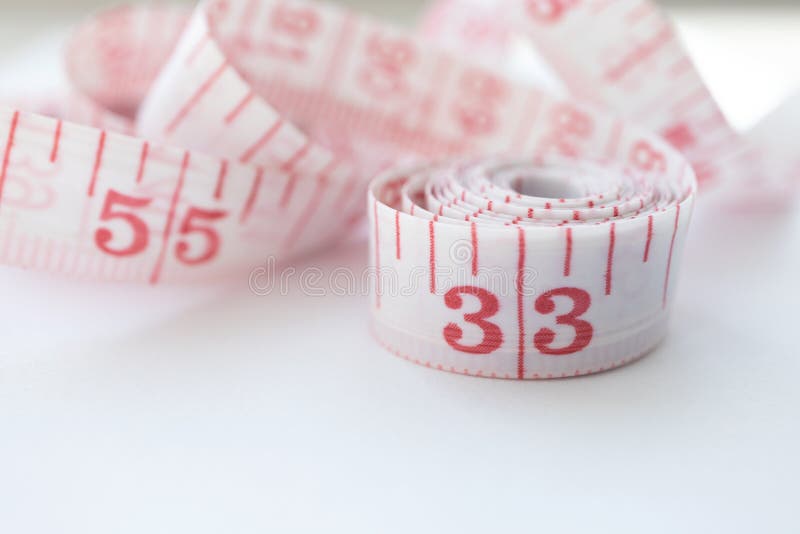 Close-up cloth tape measure with red numbers rolled up on white background. Body measure with inches