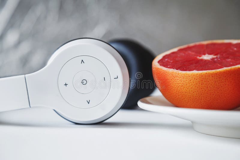 Close up composition of white minimalist headset and half of fresh red grapefruit on a small white plate