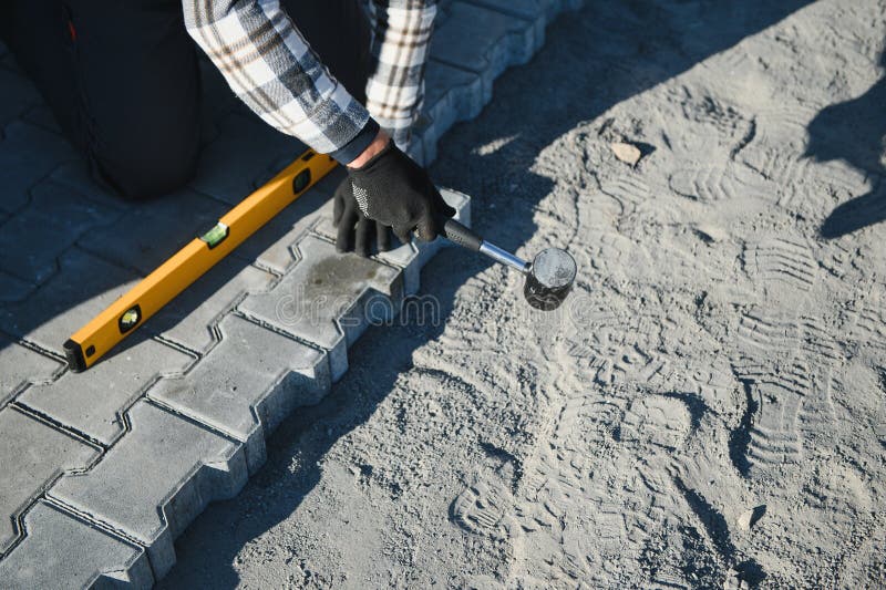 Close-up of construction worker installing and laying pavement stones on terrace, road or sidewalk. Worker using stones stock image