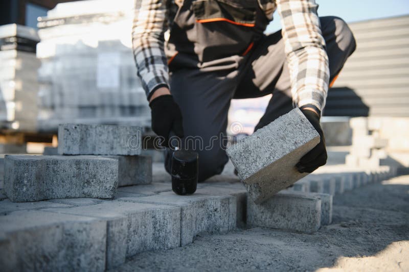 Close-up of construction worker installing and laying pavement stones on terrace, road or sidewalk. Worker using stones stock photography
