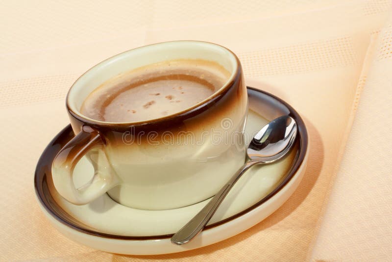 Close-up of a cup of coffee with the spoon, on ceramic plate