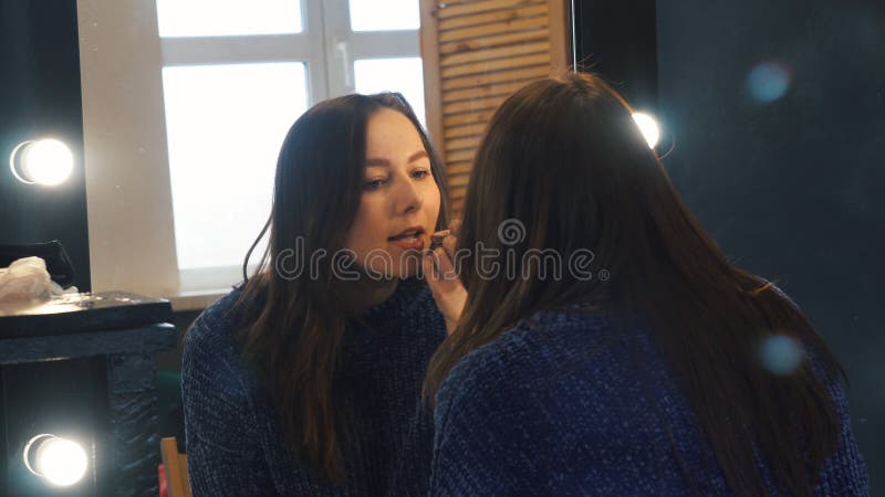 Close-up da jovem mulher bonita em escuro - posi??o azul da liga??o em ponte na frente do grande espelho e pintura de seus bordos fotografia de stock royalty free Close-up da jovem mulher bonita em escuro - posi??o azul da liga??o em ponte na frente do grande espelho e pintura de seus bordos fotografia de stock royalty free