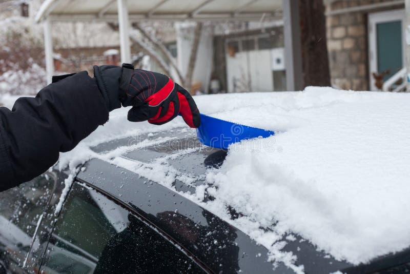 Close up da mão do homem na neve limpa das luvas do inverno do telhado do carro com dia de inverno frio da pá pequena imagem de stock Close up da mão do homem na neve limpa das luvas do inverno do telhado do carro com dia de inverno frio da pá pequena imagem de stock