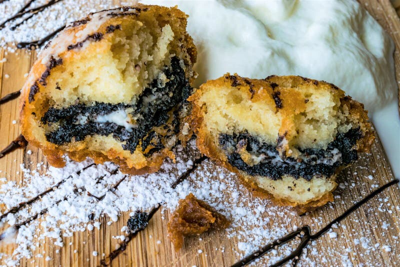 Two portions of deep fried Oreo cookies on confectioner`s sugar, strips of chocolate syrup and cream in wooden background. Two portions of deep fried Oreo cookies on confectioner`s sugar, strips of chocolate syrup and cream in wooden background