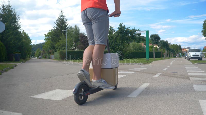 CLOSE UP: Delivery guy rides an electric scooter down sidewalk with two packages stock images