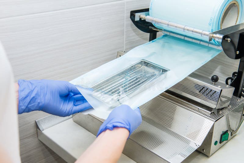 Close up dentist`s assistant hands in gloves packing dental instrument set for autoclaving in a plastic bag using vacuum packing