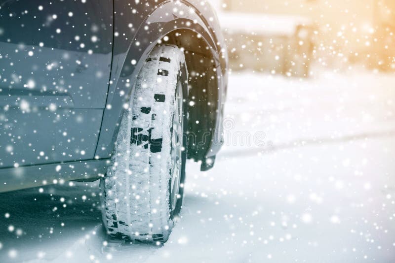 Close up detail car wheel with new black rubber tire protector on winter snow covered road. Transportation and safety concept