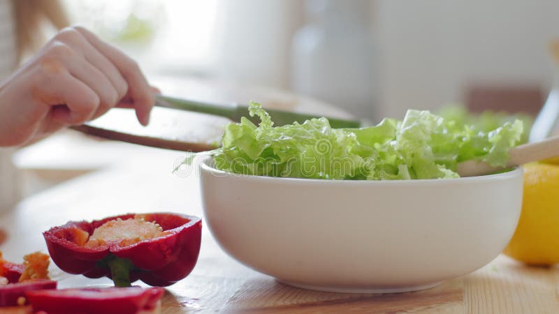 Close-up detail, cropped shooting female hands unrecognizable teen girl in apron cooks salad puts green lettuce leaves