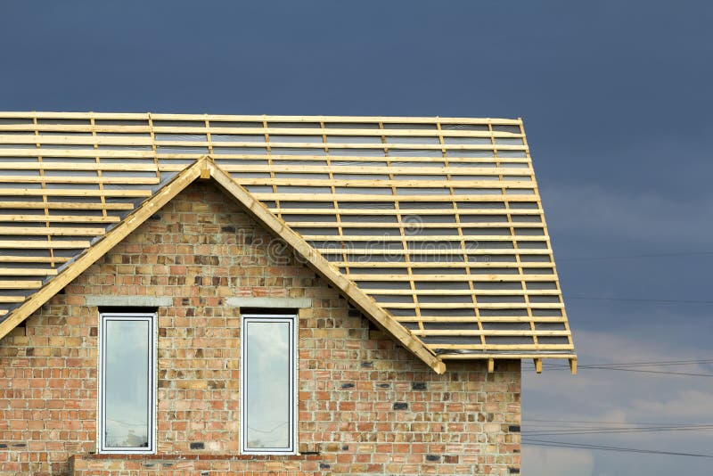 Close-up detail of new brick house top with two narrow plastic attic windows and wooden roof frame under construction on dark blue royalty free stock photo Close-up detail of new brick house top with two narrow plastic attic windows and wooden roof frame under construction on dark blue royalty free stock photo