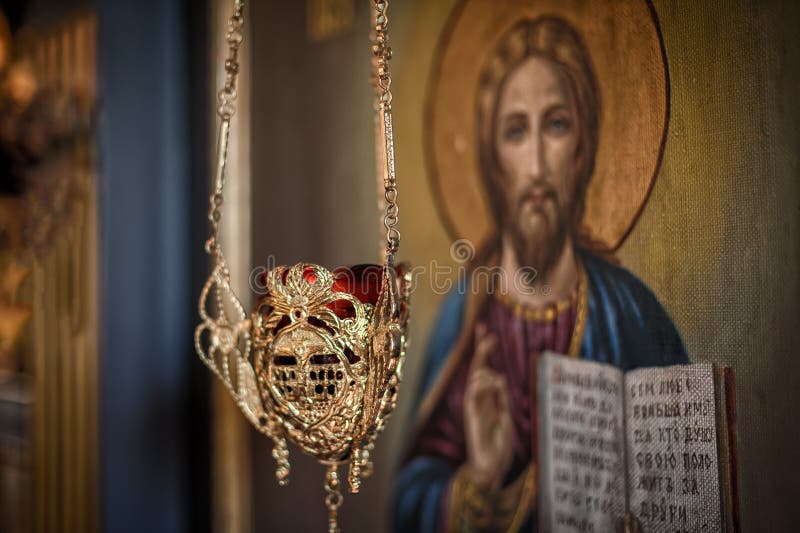 Hanging oil candle in church in front of religious iconography