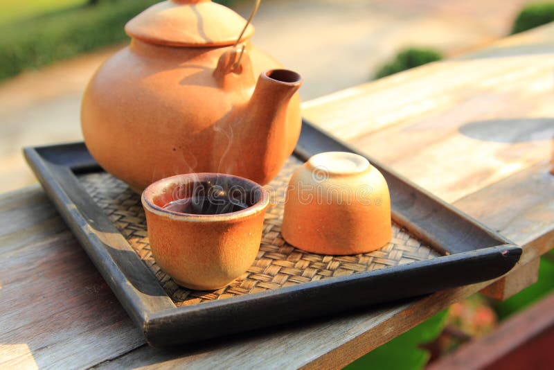 Close up earthenware teapot with pouring hot tea in a brown cup are placed on the table for healthy drinking in morning