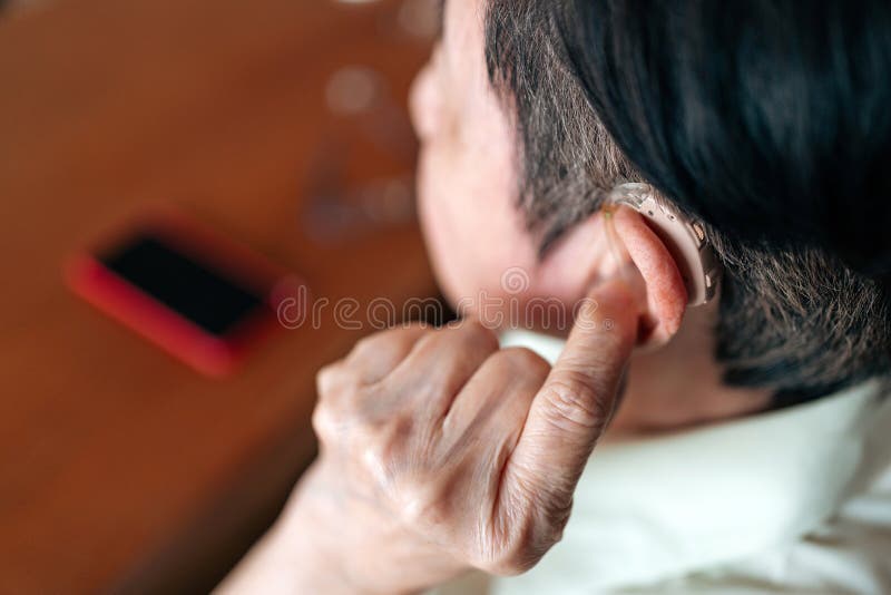Close-up of elderly person adjusting a hearing aid behind the ear, promoting hearing assistance, independence, and daily life ease royalty free stock photography