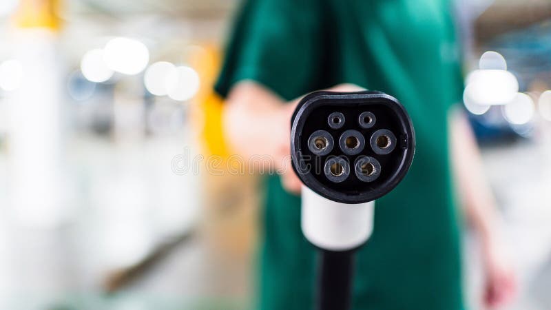 Close-up of an electric vehicle charging plug held by a person in a parking garage. Representing clean energy, EV infrastructure, sustainable transport, renewable power, and green mobility. Development ev stock images, royalty-free photos and pictures