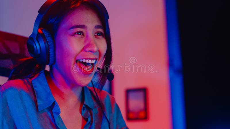 Happy asia girl gamer wear headphone competition play video game online  with smartphone colorful neon lights in living room at home. Esport  streaming game online, Home quarantine activity concept. Stock Photo