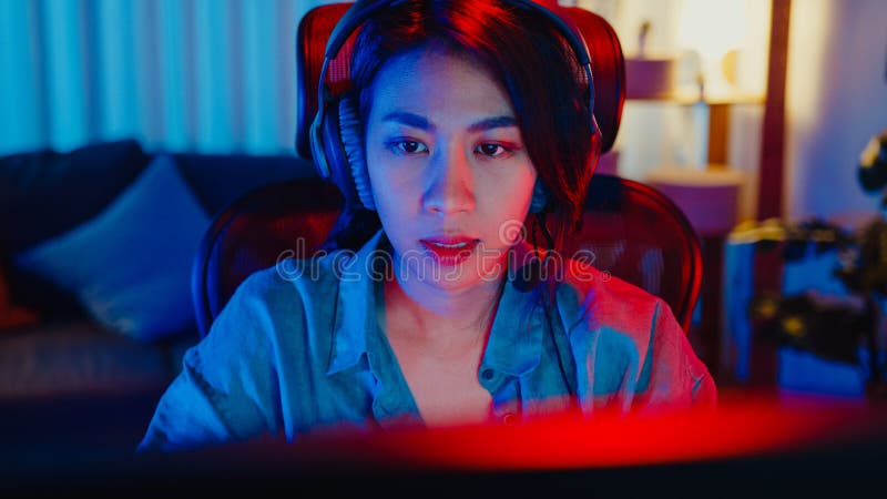 Happy asia girl gamer wear headphone competition play video game online  with smartphone colorful neon lights in living room at home. Esport  streaming game online, Home quarantine activity concept. Stock Photo