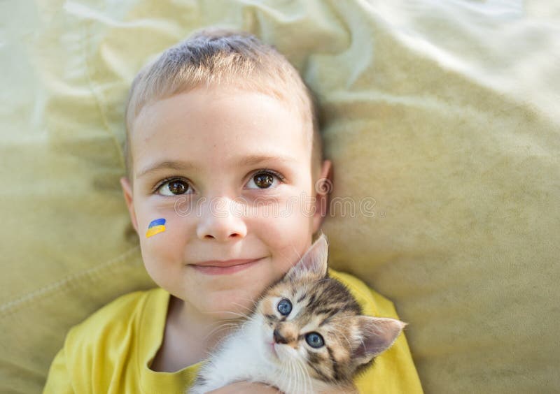 close-up of the face of a 3-year-old boy with a painted flag of Ukraine on his cheek and cute kitten muzzle