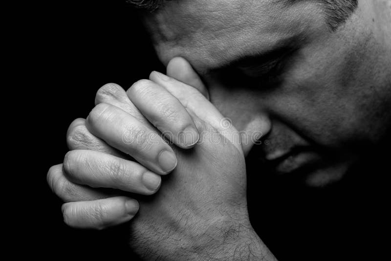 Close up of faithful mature man praying, hands folded in worship to god with head down and eyes closed in religious fervor. Black background. Concept for religion, faith, prayer and spirituality.