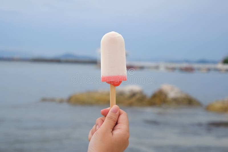 Close up of a female hand holding ice cream Two tone isolated on blurred nature background. Close up of a female hand holding ice cream Two tone isolated on blurred nature background