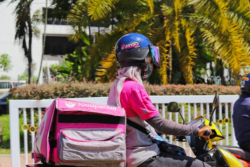 Side and close-up view of a Malay female Foodpanda delivery rider out on the streets of Ipoh, Malaysia . The woman`s face is not visible being shielded by the visor mounted on the helmet. Also, she has a `BUDAK PANDA PERAK` sticker on her crash helmet. Side and close-up view of a Malay female Foodpanda delivery rider out on the streets of Ipoh, Malaysia . The woman`s face is not visible being shielded by the visor mounted on the helmet. Also, she has a `BUDAK PANDA PERAK` sticker on her crash helmet