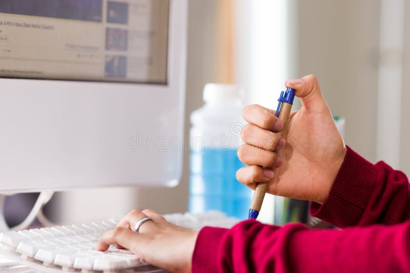 Close-up of a female hand holding a pen in a desk with a computer. fiddling concept stock photo