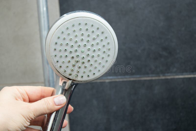 Close up of a female hand holding a shower head with limescale stains in the shower royalty free stock photography