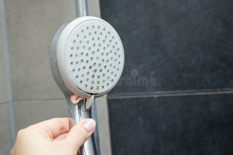 Close up of a female hand holding a shower head with limescale stains in the shower royalty free stock photography