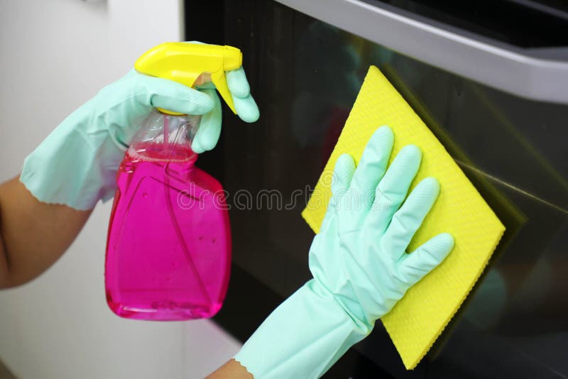 Close up of female hands with protective gloves cleaning oven door. Girl polishing kitchen. People, housework, cleaning concept.