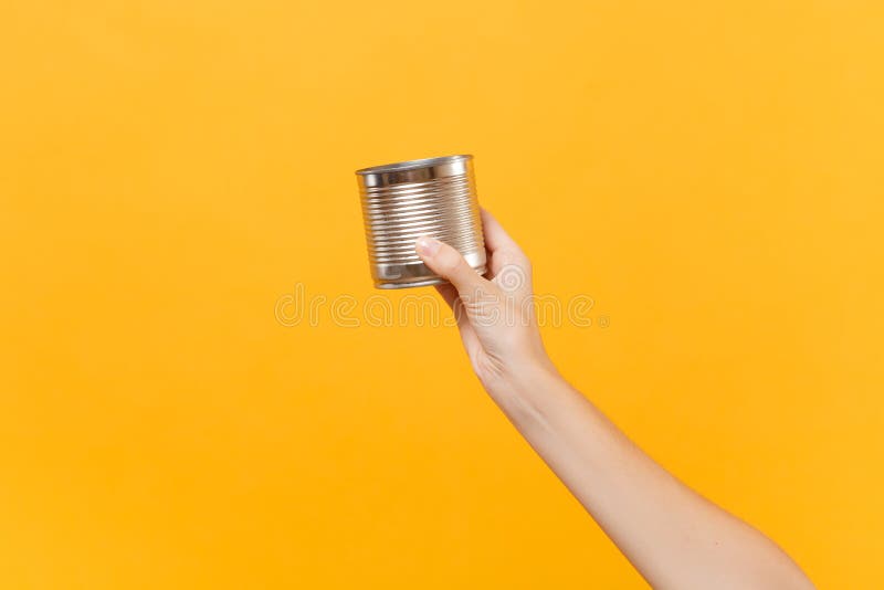 Close up female hold in hand clear empty blank iron metal chrome can canned goods food isolated on yellow background royalty free stock image Close up female hold in hand clear empty blank iron metal chrome can canned goods food isolated on yellow background royalty free stock image