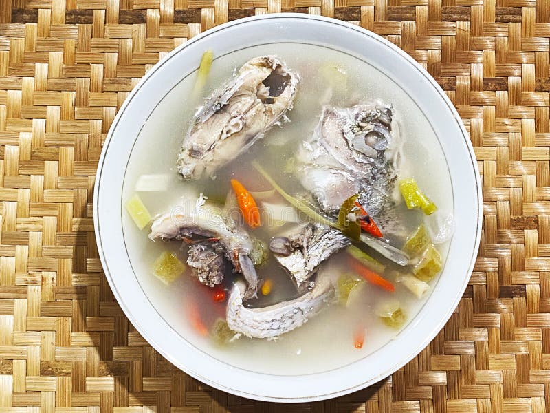 Close-up of fish soup with chilli and vegetables. Close-up of fish soup on white bowl with chilli and vegetables isolated on bamboo texture background