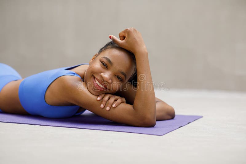 Close up of fit young female lying on exercise mat in gym and smiling. Healthy woman taking break after workout in gym.