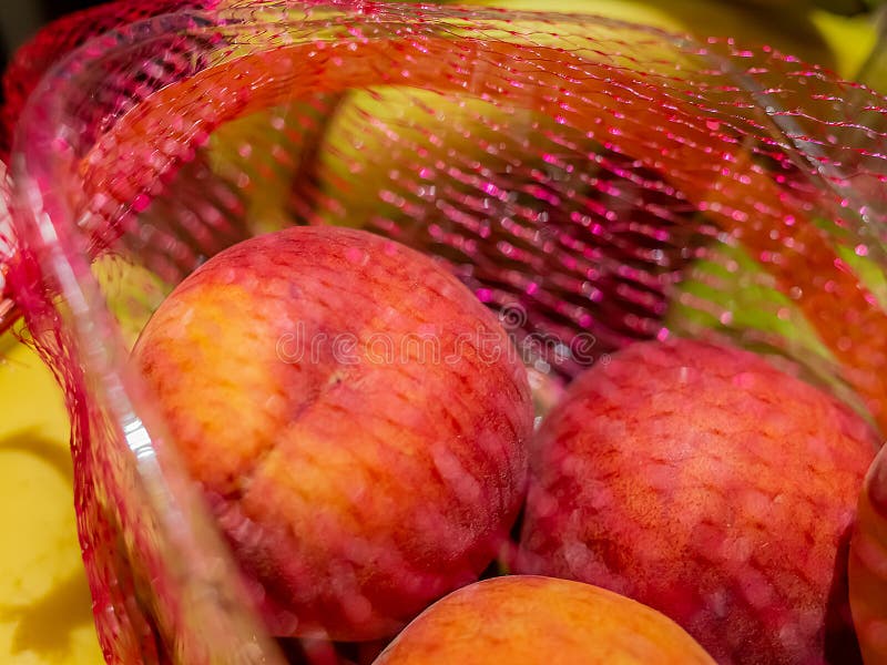 Fresh peaches in a plastic container surrounded by red netting