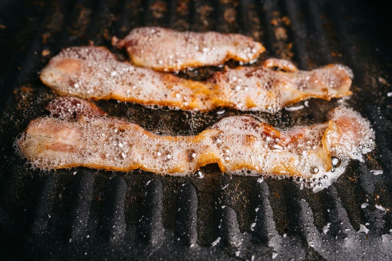 A close up view of bacon sizzling in the frying pan on a stovetop. Cooking  bacon slices for breakfast fry up Stock Photo - Alamy