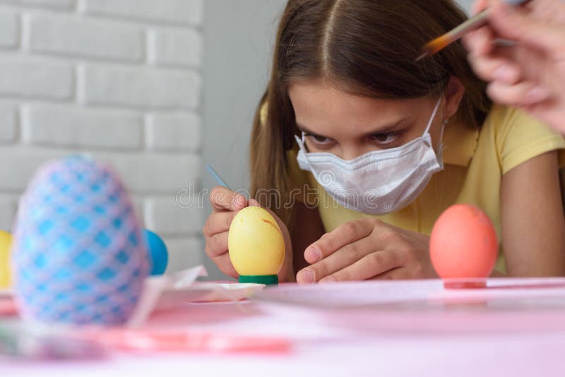 Close-up of a girl in a medical mask who paints Easter  eggs