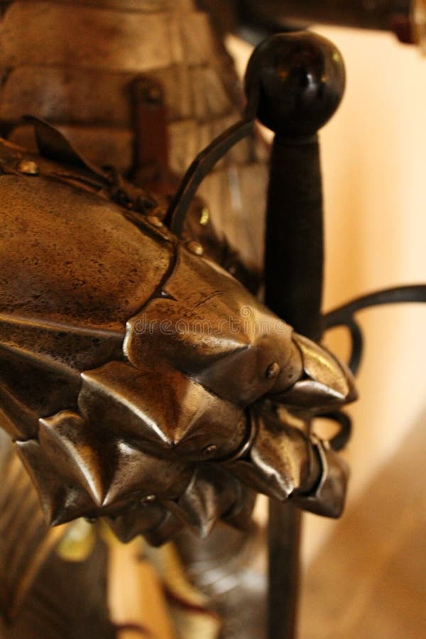 Close up of a glove from an old knight armor. Close up of a metal glove from the middle ages. The fingers enclose a sword which conveys both safety and danger stock photography Close up of a glove from an old knight armor. Close up of a metal glove from the middle ages. The fingers enclose a sword which conveys both safety and danger stock photography