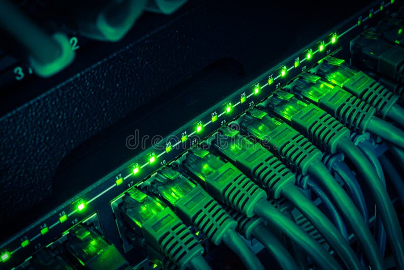 Close up of green network cables from data center connected with patch cord to black switch glowing in the dark stock photo