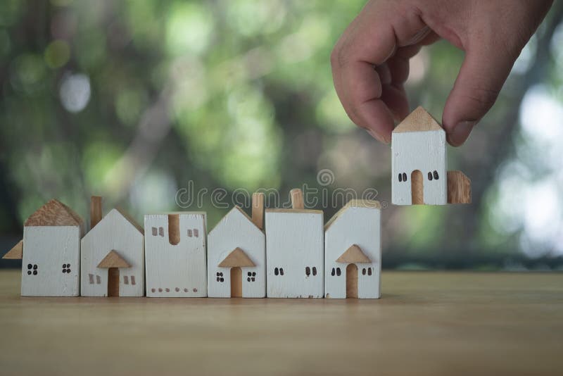 Close up hand choosing mini wood house model from a row model against nature background