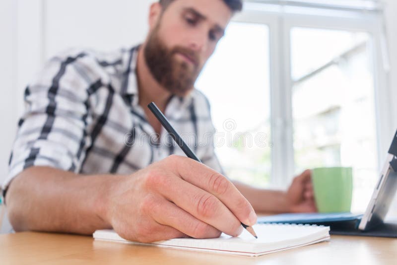 Close-up of the hand of a creative young man holding a pencil over a blank notebook, while thinking of a new project or assignment during freelance work in a co-working space. Close-up of the hand of a creative young man holding a pencil over a blank notebook, while thinking of a new project or assignment during freelance work in a co-working space