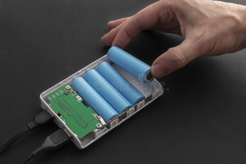 Close-up of a hand inserting a 18650 lithium battery into a disassembled power bank stock photo