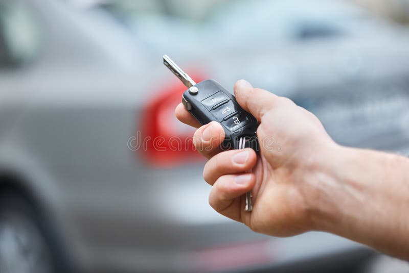 Close up hand of Man holding car key  with blurred car on background. hand presses on the remote control car alarm systems.