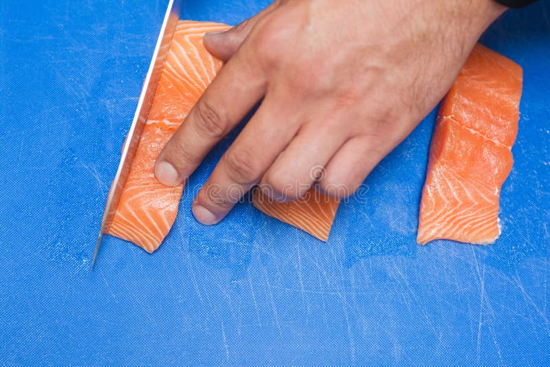Close Up of Hand Slicing Raw Salmon with Sharp Knife Stock Photo