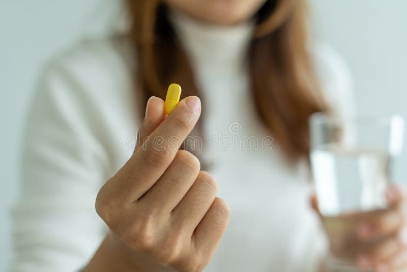 Close up of hand of woman holding a dietary supplement or medication or vitamin and a glass of water ready to take.