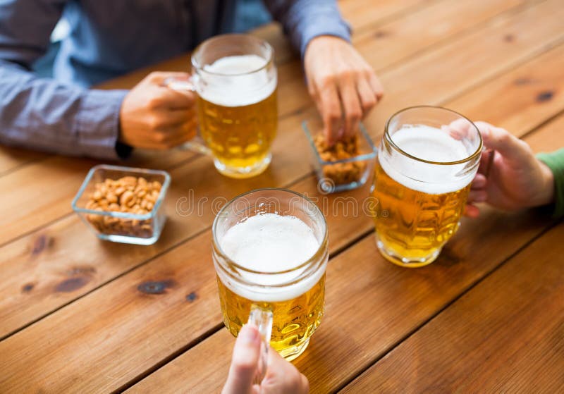 Close up of hands with beer mugs at bar or pub