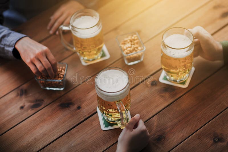 Close up of hands with beer mugs at bar or pub