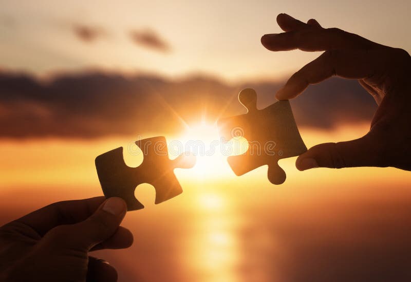 Close up of hands connecting two pieces of jigsaw puzzle