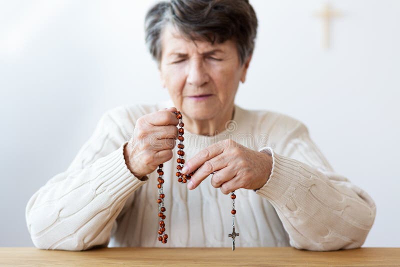 Close-up on the hands of a focused grandmother praying with a re stock photography Close-up on the hands of a focused grandmother praying with a re stock photography